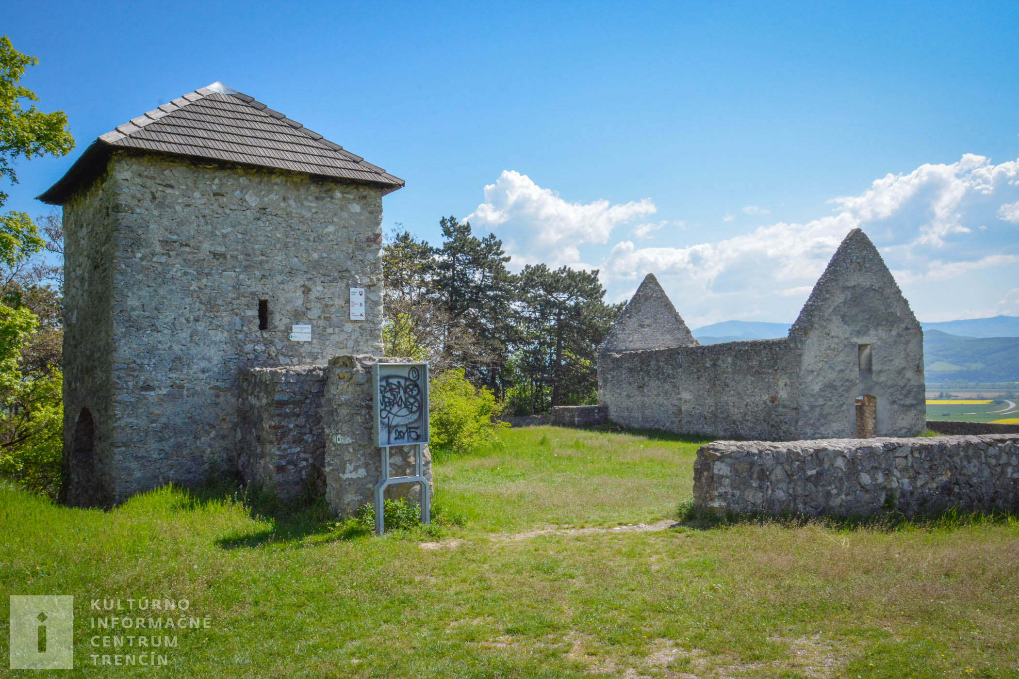 Vľavo sa nachádza z časti obnovená strážna veža a vpravo pozostatky románskeho kostolíka v Haluziciach